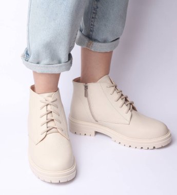 Kot pantolonlu kadın bacakları ve beyaz arka planda beyaz deri çizmeler. Moda konsepti