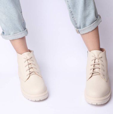 Kot pantolonlu kadın bacakları ve beyaz arka planda beyaz deri çizmeler. Moda konsepti