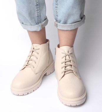 Kot pantolonlu kadın bacakları ve beyaz arka planda beyaz deri çizmeler. Moda konsepti