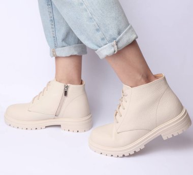 Kot pantolonlu kadın bacakları ve beyaz arka planda beyaz deri çizmeler. Moda konsepti