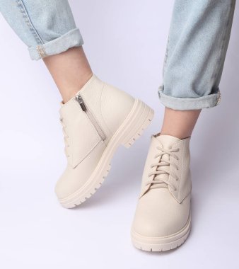 Kot pantolonlu kadın bacakları ve beyaz arka planda beyaz deri çizmeler. Moda konsepti