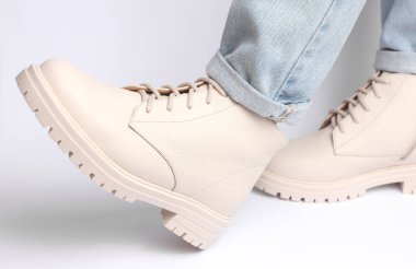 Kot pantolonlu kadın bacakları ve beyaz arka planda beyaz deri çizmeler. Moda konsepti