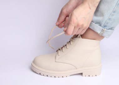 Beyaz arka planda beyaz deri ayakkabıların bağcıklarını bağlayan kadın elleri