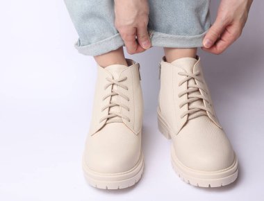 Kot pantolonlu kadın bacakları ve beyaz arka planda beyaz deri çizmeler. Moda konsepti