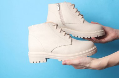 Mavi arka planda beyaz deri çizme tutan kadın eller.