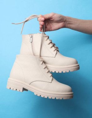 Kadının eli mavi arka planda beyaz deri bir çizme tutuyor.