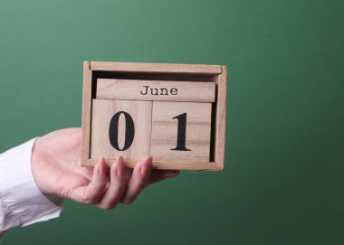 1 Haziran tarihli ahşap blok takvimini yeşil arka planda tutan bir el.