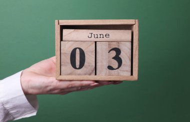 3 Haziran tarihli ahşap blok takvimini yeşil arka planda tutan el.
