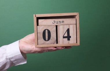 4 Haziran tarihli ahşap blok takvimini yeşil arka planda tutan el.