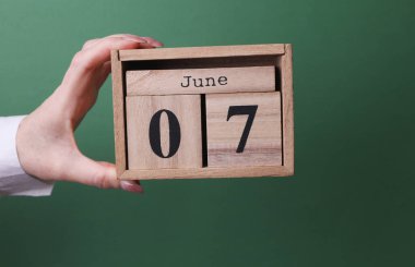 Elinde ahşap blok takvimi ile 7 Haziran 'da yeşil arka planda.