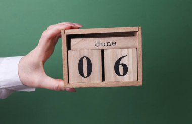 Elinde tahta blok takvimi ile 6 Haziran 'da yeşil arka planda.