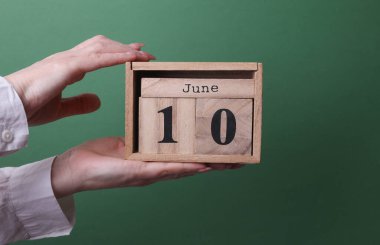 10 Haziran tarihli ahşap blok takvimini yeşil arka planda tutan bir el.