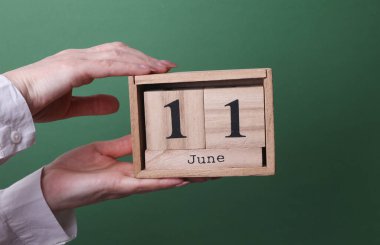 11 Haziran tarihli ahşap blok takvimini yeşil arka planda tutan el.