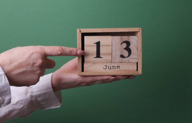 13 Haziran tarihli ahşap blok takvimini yeşil arka planda tutan el.