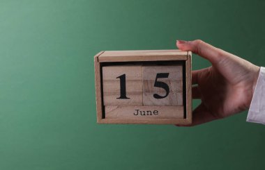 15 Haziran tarihli ahşap blok takvimini yeşil arka planda tutan el.