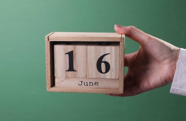 Elinde tahta blok takvimi ile 16 Haziran 'da yeşil arka planda.