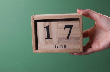 17 Haziran tarihli ahşap blok takvimini yeşil arka planda tutan el.
