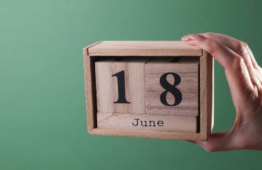 18 Haziran tarihli ahşap blok takvimini yeşil arka planda tutan bir el.