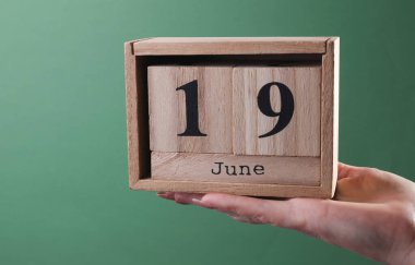 Elinde tahta blok takvimi olan, 19 Haziran 'da yeşil arka planda olan bir el.