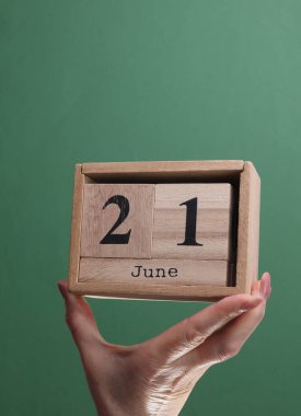 21 Haziran tarihli ahşap blok takvimini yeşil arka planda tutan bir el.