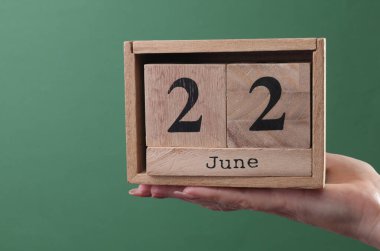 22 Haziran tarihli ahşap blok takvimini yeşil arka planda tutan bir el.