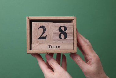 28 Haziran tarihli ahşap blok takvimini yeşil arka planda tutan bir el.