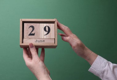 29 Haziran tarihli ahşap blok takvimini yeşil arka planda tutan bir el.