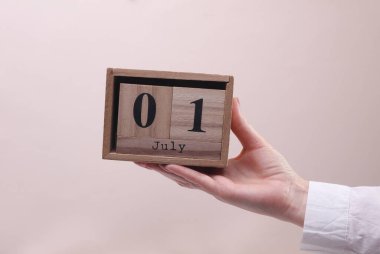 Kadın El, tahta blok takvimi tutuyor. Bej arka planda tarih 1 Temmuz.
