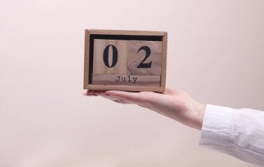 Kadın El, tahta blok takvimi tutuyor. Bej arka planda tarihi 2 Temmuz.