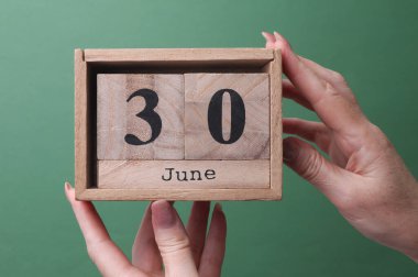30 Haziran tarihli ahşap blok takvimini yeşil arka planda tutan bir el.