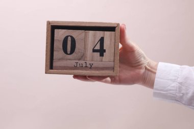 4 Temmuz tarihli tahta blok takvimi tutan kadın el bej arka planda