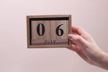 Kadın El, tahta blok takvimi tutuyor. Bej arka planda 6 Temmuz tarihi var.