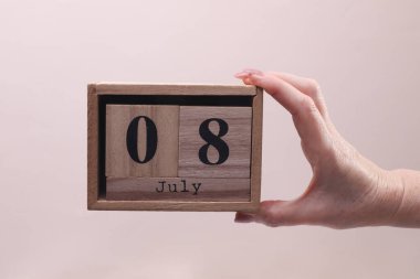 Kadın El, tahta blok takvimi tutuyor. Bej arka planda tarih 8 Temmuz.