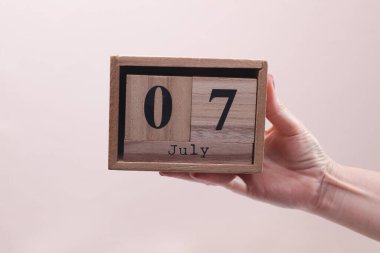 Kadın El, elinde tahta blok takvimi ile 7 Temmuz 'da bej arka planda