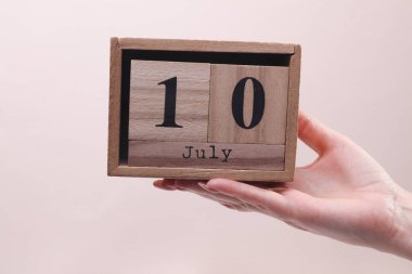 10 Temmuz tarihli tahta blok takvimi tutan kadın el bej arka planda