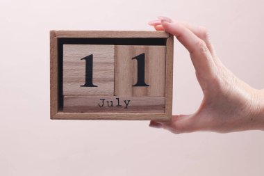11 Temmuz tarihli tahta blok takvimi tutan kadın el bej arka planda