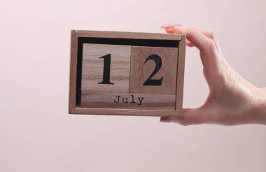12 Temmuz tarihli tahta blok takvimi tutan kadın el bej arka planda