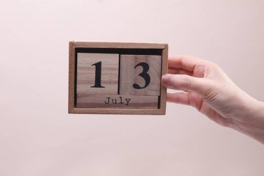 Elinde tahta blok takvimi olan 13 Temmuz tarihli kadın el bej arka planda