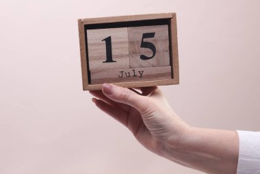 15 Temmuz tarihli tahta blok takvimi tutan kadın el bej arka planda