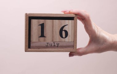 Kadın El, tahta blok takvimi tutuyor. Bej arka planda tarih 16 Temmuz.