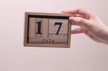 17 Temmuz tarihli ahşap blok takvimi tutan kadın el bej arka planda