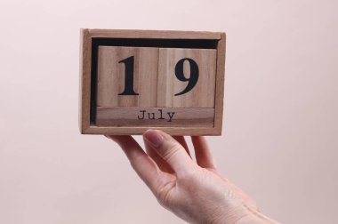 Kadın El, elinde tahta blok takvimi ile 19 Temmuz 'da bej arka planda