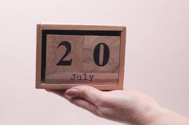 Kadın El, tahta blok takvimi tutuyor. Bej arka planda tarih 20 Temmuz.