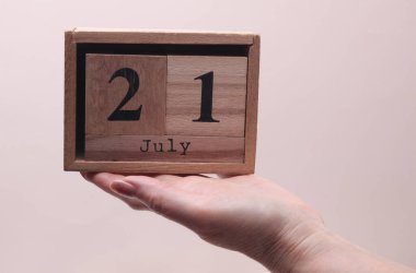 Kadın El, tahta blok takvimi tutuyor. Bej arka planda 21 Temmuz tarihi var.
