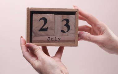 23 Temmuz tarihli tahta blok takvimi tutan kadın el bej arka planda