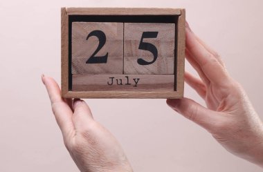 25 Temmuz tarihli tahta blok takvimi tutan kadın el bej arka planda