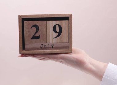 29 Temmuz tarihli tahta blok takvimi tutan kadın el bej arka planda