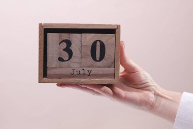 Beyaz arka planda 30 Temmuz tarihli tahta blok takvimi tutan kadın el.