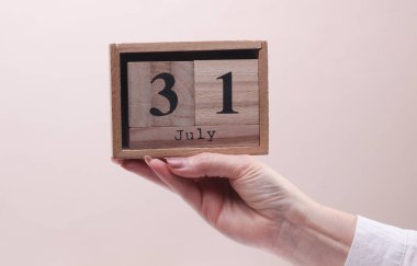 Beyaz arka planda 31 Temmuz tarihli tahta blok takvimi tutan kadın el.