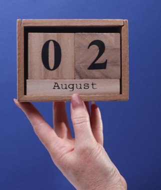 2 Ağustos tarihli ahşap blok takvimi tutan kadın el mavi arka planda